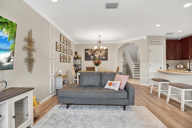 living room with crown molding, an inviting chandelier, and light hardwood / wood-style floors