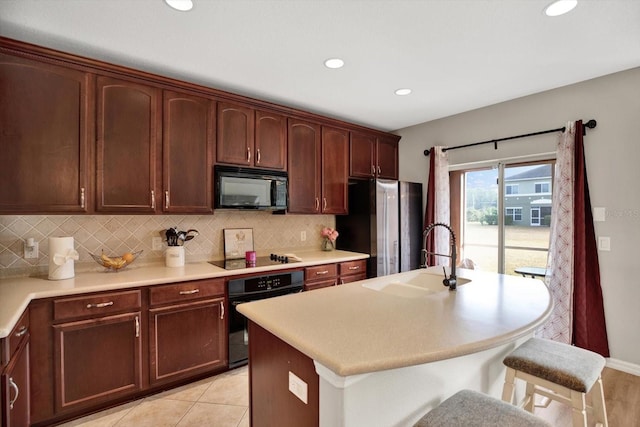 kitchen featuring sink, a kitchen island with sink, backsplash, a kitchen breakfast bar, and black appliances