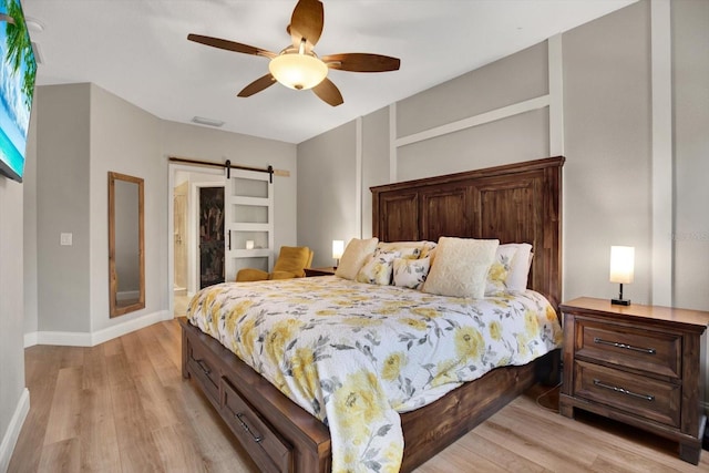 bedroom featuring a barn door, ceiling fan, and light hardwood / wood-style flooring