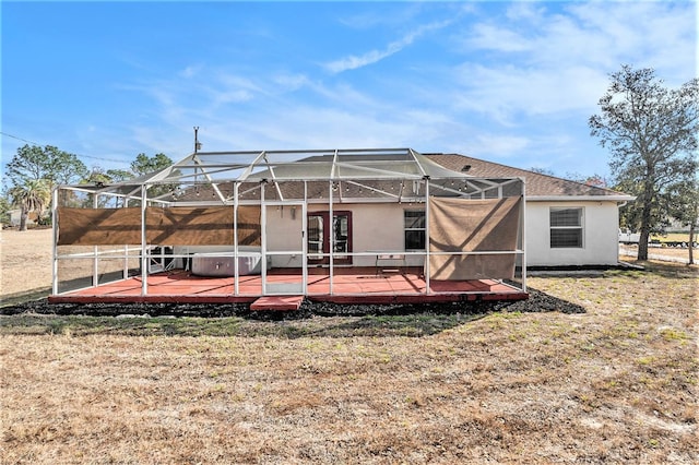 back of property with a hot tub, a wooden deck, a lanai, and a lawn