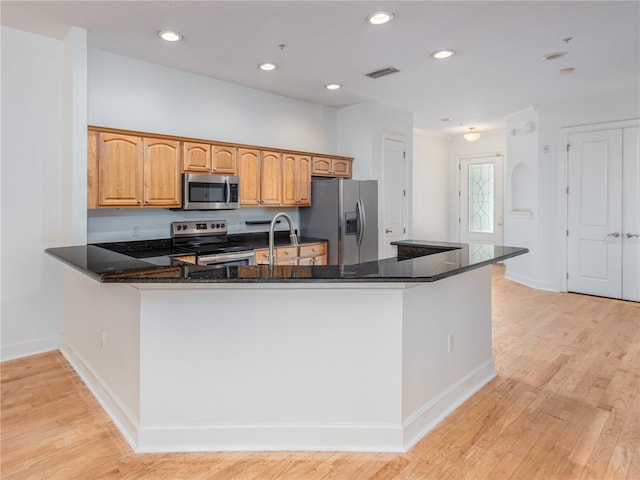 kitchen featuring stainless steel appliances, kitchen peninsula, sink, and dark stone countertops