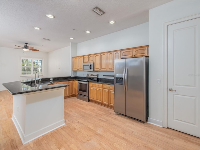 kitchen featuring sink, dark stone counters, kitchen peninsula, stainless steel appliances, and light wood-type flooring