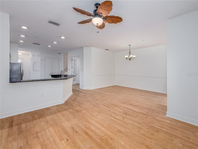 unfurnished living room featuring sink, ceiling fan with notable chandelier, and light hardwood / wood-style floors