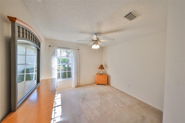 empty room with ceiling fan, light carpet, and a textured ceiling