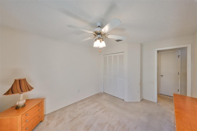 unfurnished bedroom with a textured ceiling, light colored carpet, a closet, and ceiling fan