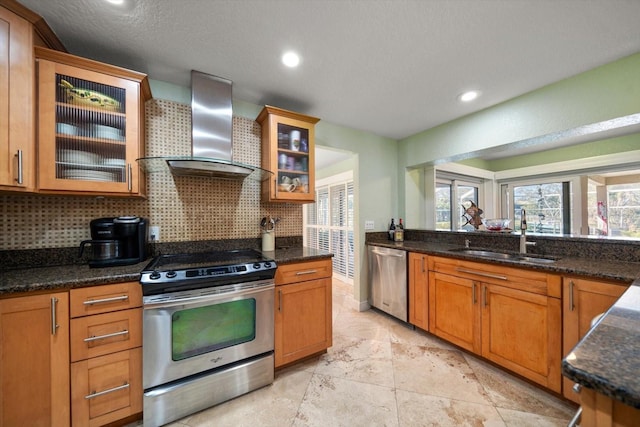 kitchen featuring appliances with stainless steel finishes, sink, decorative backsplash, dark stone counters, and wall chimney exhaust hood