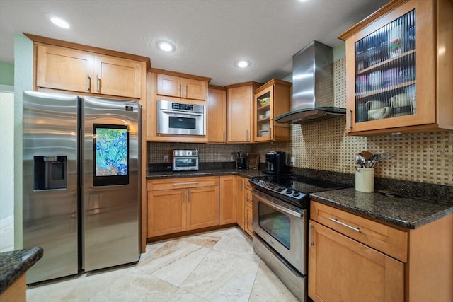 kitchen featuring appliances with stainless steel finishes, backsplash, dark stone counters, and wall chimney exhaust hood