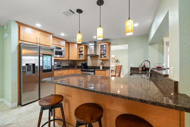 kitchen featuring sink, a breakfast bar, appliances with stainless steel finishes, kitchen peninsula, and wall chimney exhaust hood