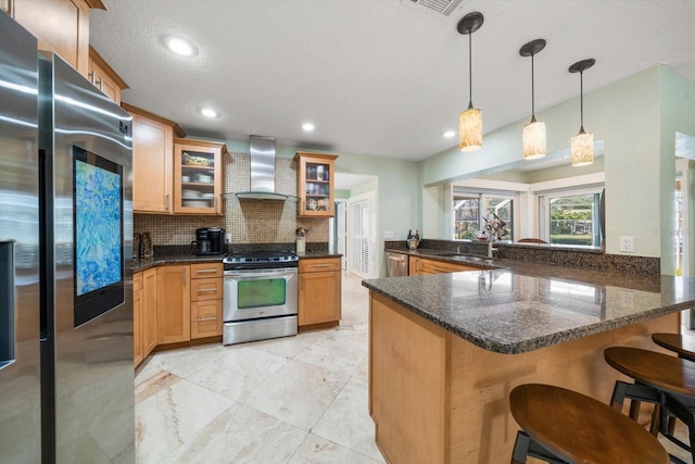 kitchen with appliances with stainless steel finishes, decorative light fixtures, tasteful backsplash, kitchen peninsula, and wall chimney range hood