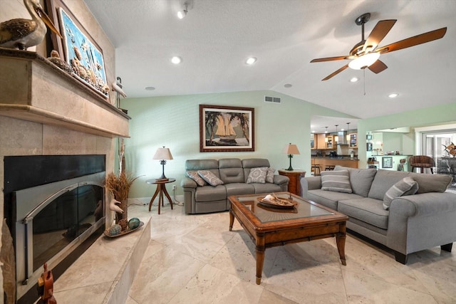 living room with lofted ceiling, ceiling fan, a tiled fireplace, and a textured ceiling