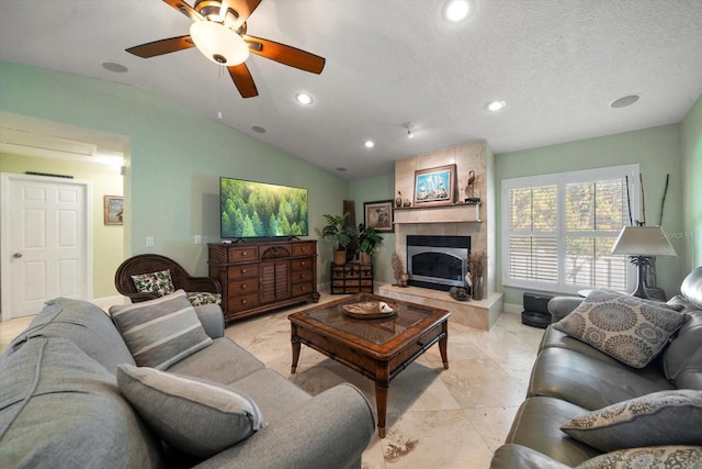 living room featuring a tiled fireplace, ceiling fan, vaulted ceiling, and a textured ceiling