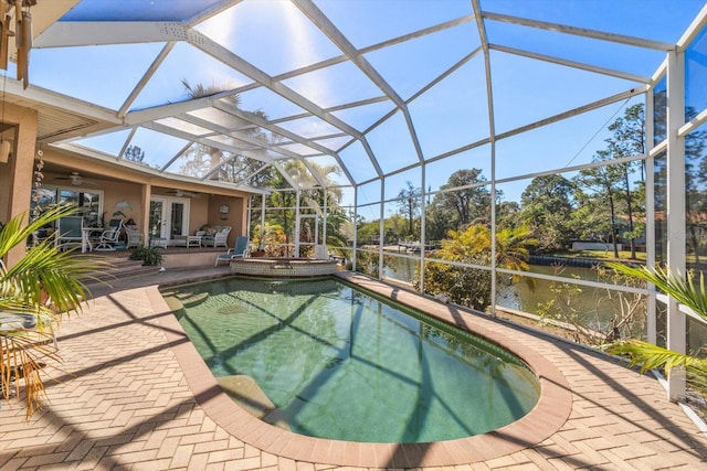 view of pool with french doors, a water view, a lanai, ceiling fan, and a patio