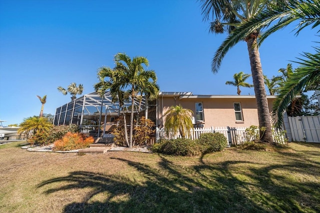 rear view of property featuring glass enclosure and a lawn