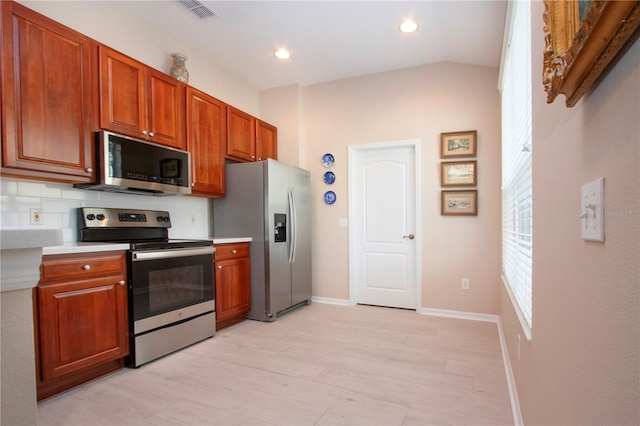 kitchen with vaulted ceiling, appliances with stainless steel finishes, backsplash, and light wood-type flooring