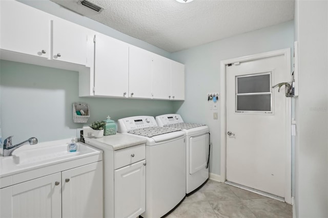 laundry area featuring washing machine and clothes dryer, sink, cabinets, a textured ceiling, and light tile patterned floors