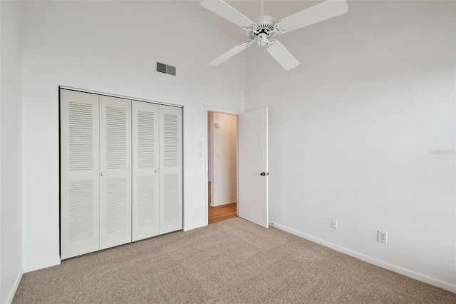 unfurnished bedroom featuring carpet, a towering ceiling, ceiling fan, and a closet