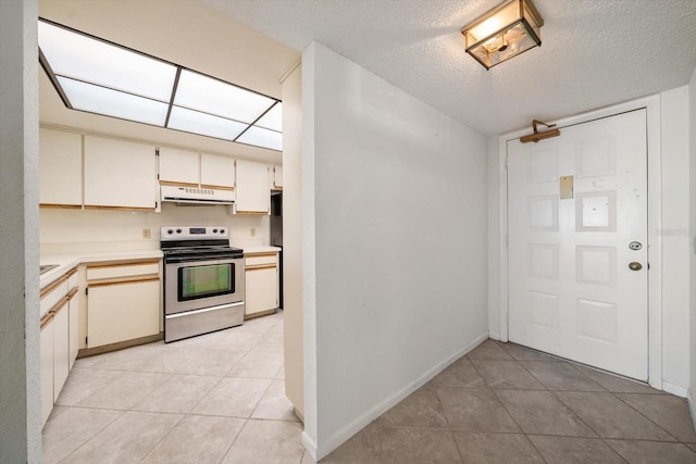 kitchen with light tile patterned floors, electric range, cream cabinets, and a textured ceiling