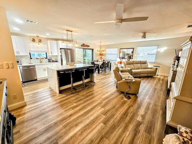 living room with ceiling fan with notable chandelier and light hardwood / wood-style floors