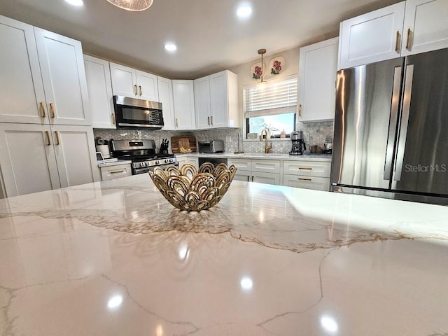 kitchen with light stone counters, decorative backsplash, stainless steel appliances, and white cabinets