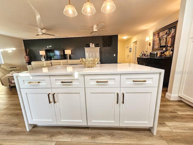 kitchen with white cabinetry, light stone counters, light wood-type flooring, pendant lighting, and ceiling fan