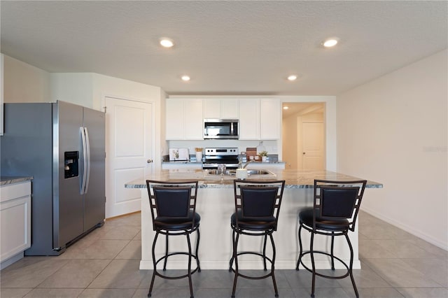 kitchen with light stone counters, appliances with stainless steel finishes, an island with sink, and white cabinets