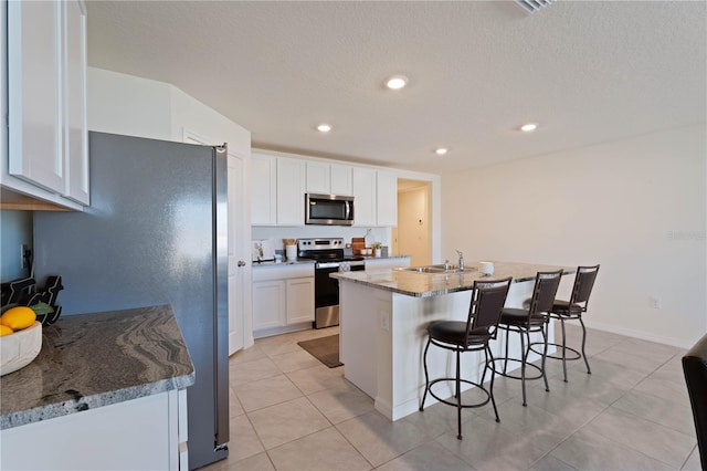 kitchen with sink, stainless steel appliances, light stone countertops, white cabinets, and a center island with sink