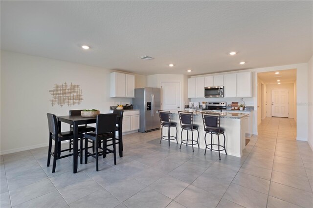 kitchen featuring appliances with stainless steel finishes, a breakfast bar, a center island with sink, and white cabinets