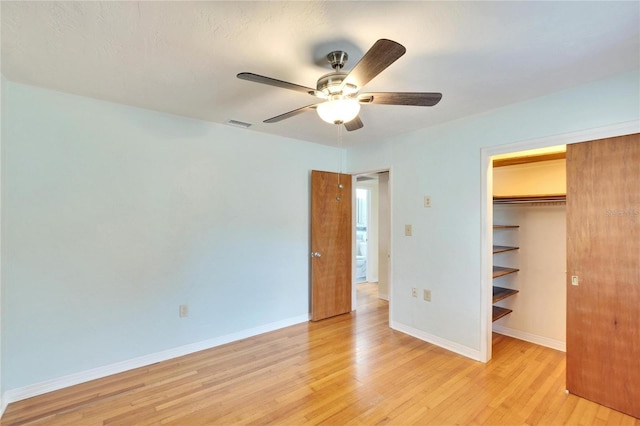 unfurnished bedroom with ceiling fan, a walk in closet, a closet, and light wood-type flooring