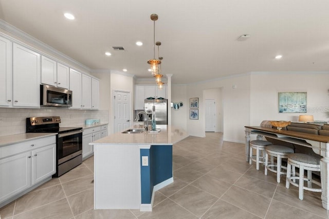 kitchen with sink, stainless steel appliances, white cabinets, a center island with sink, and decorative light fixtures