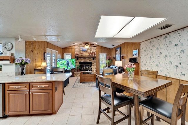 dining space with visible vents, a textured ceiling, light tile patterned flooring, a brick fireplace, and ceiling fan