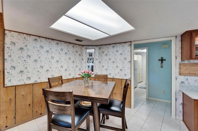 dining area with light tile patterned floors, a wainscoted wall, visible vents, and wallpapered walls