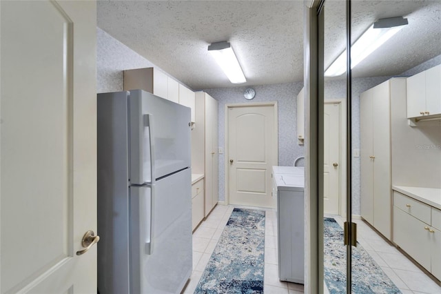 kitchen featuring light tile patterned flooring, freestanding refrigerator, light countertops, a textured ceiling, and white cabinetry