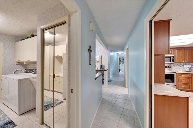 laundry area with light tile patterned floors, washer and clothes dryer, cabinets, and a textured ceiling