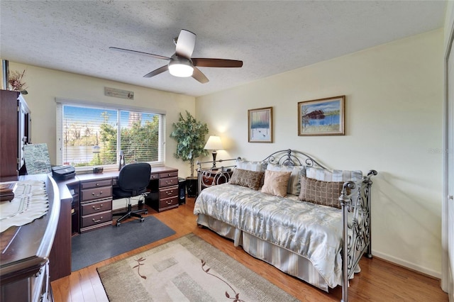 bedroom with ceiling fan, wood finished floors, baseboards, and a textured ceiling