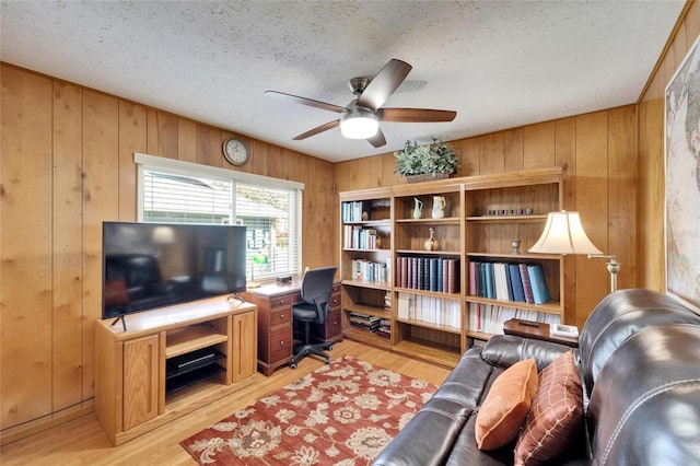 office area featuring ceiling fan, light wood-style flooring, wood walls, and a textured ceiling