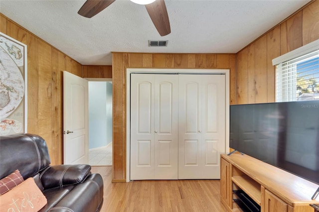 living room featuring ceiling fan, light hardwood / wood-style flooring, a textured ceiling, and wood walls