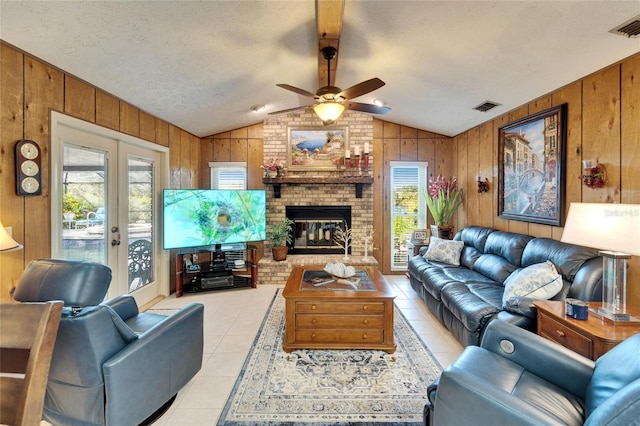 living room with a brick fireplace, wood walls, lofted ceiling with beams, light tile patterned floors, and french doors