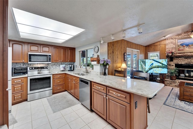 kitchen featuring a sink, appliances with stainless steel finishes, a peninsula, a fireplace, and light stone countertops