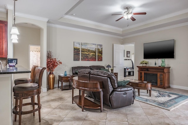 tiled living room with a tray ceiling, ornamental molding, and ceiling fan