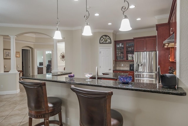 kitchen with crown molding, hanging light fixtures, stainless steel refrigerator with ice dispenser, dark stone counters, and ornate columns