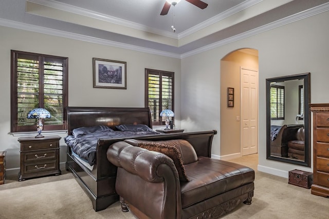 bedroom featuring a raised ceiling, ornamental molding, light colored carpet, and ceiling fan