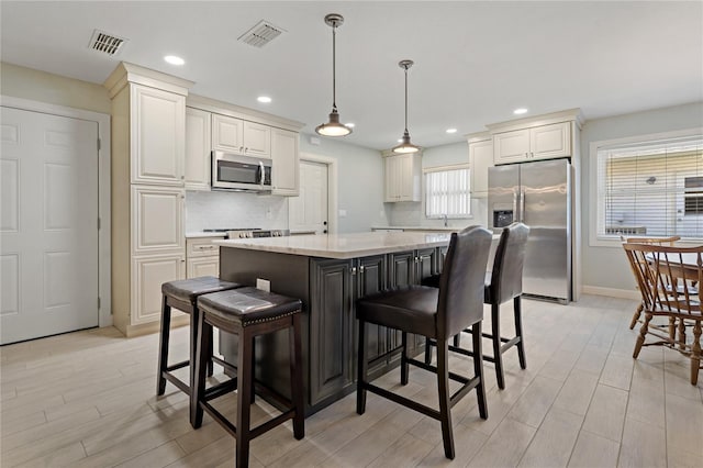 kitchen featuring a kitchen island, appliances with stainless steel finishes, tasteful backsplash, a kitchen breakfast bar, and hanging light fixtures