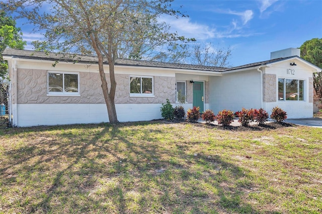 ranch-style house with a shingled roof, concrete block siding, and a front lawn