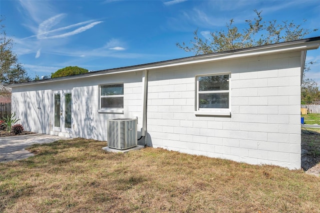 rear view of house with a yard, central AC unit, and concrete block siding