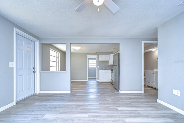 unfurnished living room with ceiling fan, sink, a textured ceiling, and light wood-type flooring