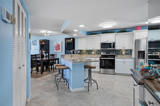 kitchen with white cabinets, decorative backsplash, light stone counters, appliances with stainless steel finishes, and a breakfast bar