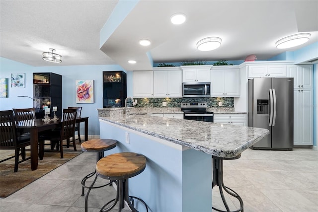 kitchen featuring stainless steel appliances, a peninsula, white cabinets, a kitchen breakfast bar, and backsplash