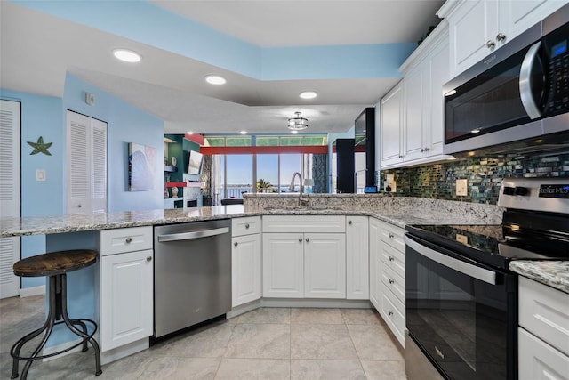 kitchen with backsplash, appliances with stainless steel finishes, white cabinets, a sink, and a peninsula