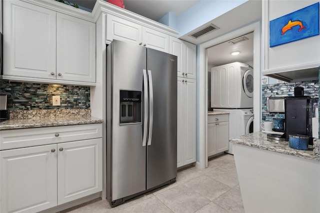 kitchen featuring stainless steel refrigerator with ice dispenser, stacked washer and dryer, tasteful backsplash, visible vents, and white cabinets