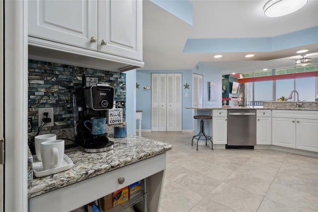 kitchen with a sink, white cabinetry, baseboards, stainless steel dishwasher, and light stone countertops